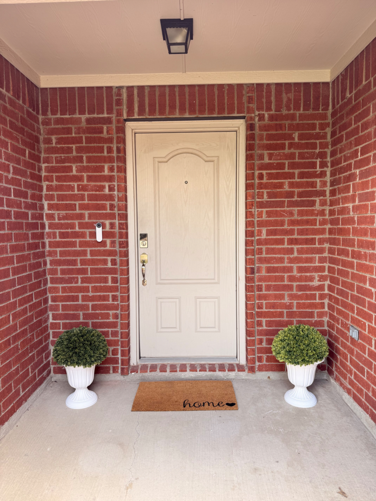 Covered front porch with topiaries and a home doormat