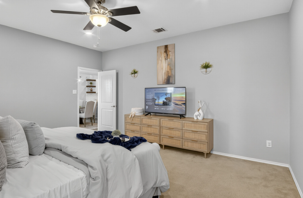 Bedroom with dresser, mounted TV and ceiling fan